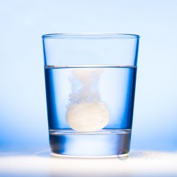 glass with water on blue background with a dissolving pill